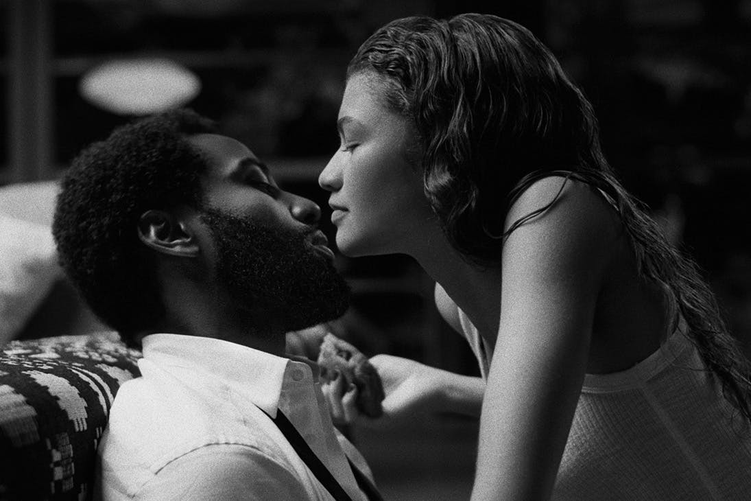 a black and white image of a young woman leaning in to a kiss a man on a couch.